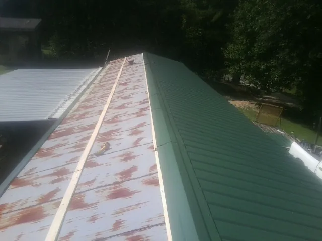Old rusted panels beside newly installed green metal roofing — Wind Damage Roof Repair by Roofing Brothers in Hesston