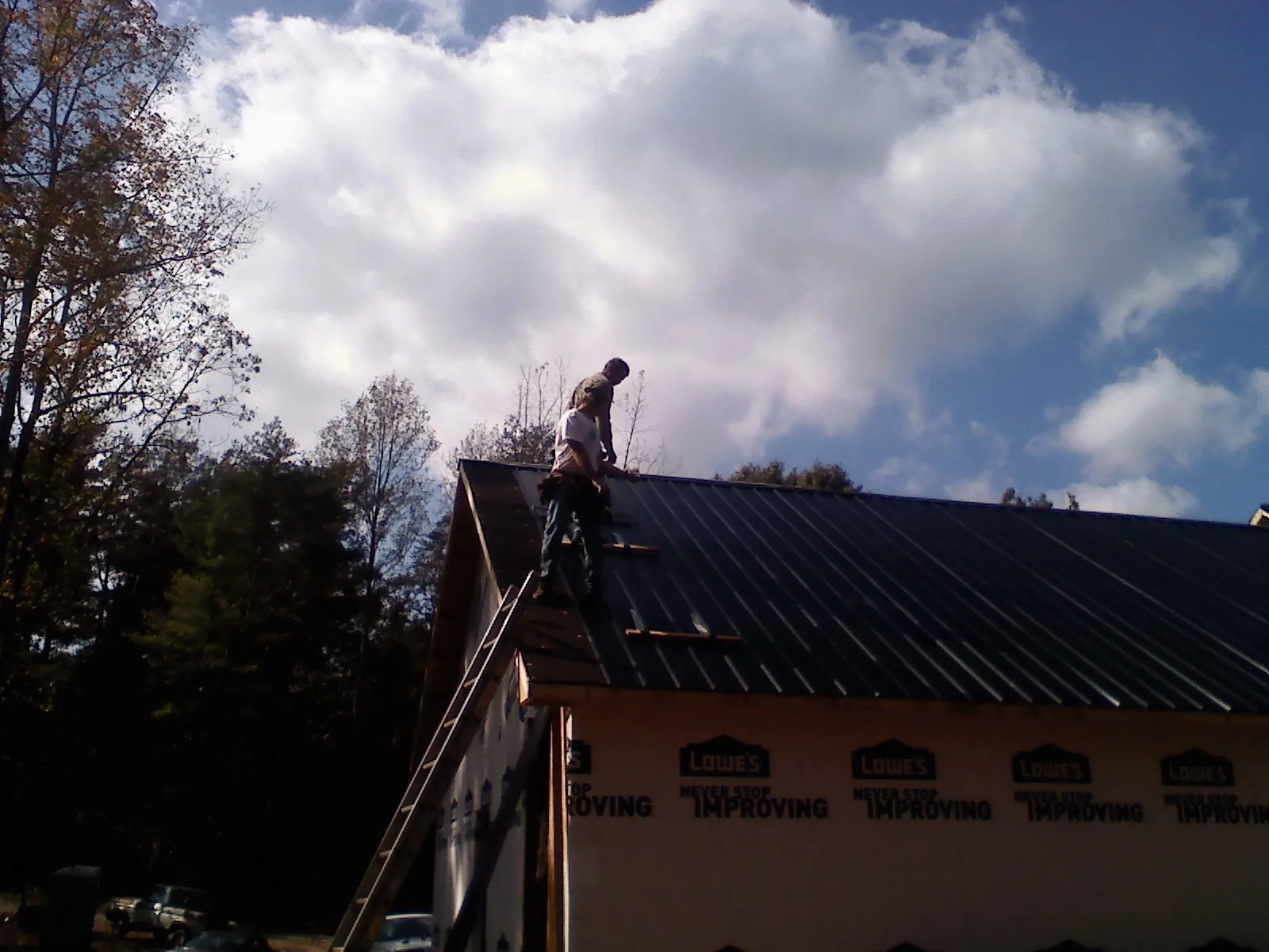 Roofer fastening dark metal panels high against a cloudy sky, from a Roof Inspection job in Hesston